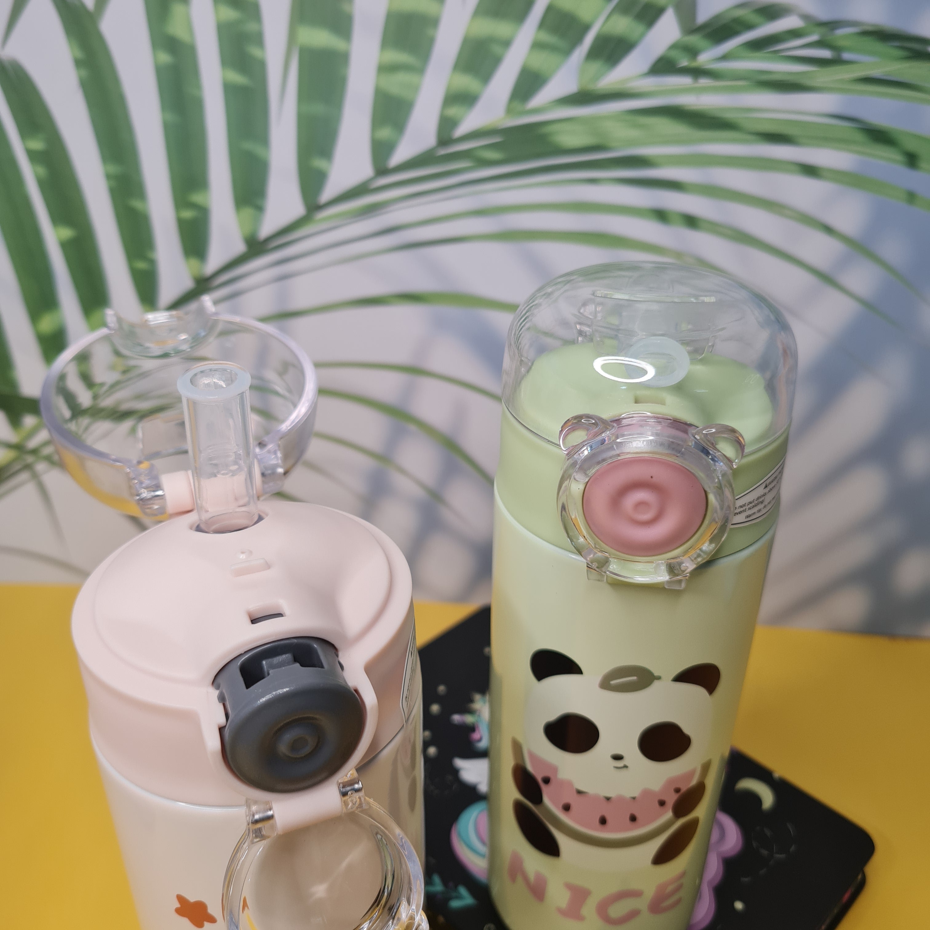 Two colorful water bottles with unique designs on a surface with a leafy background.